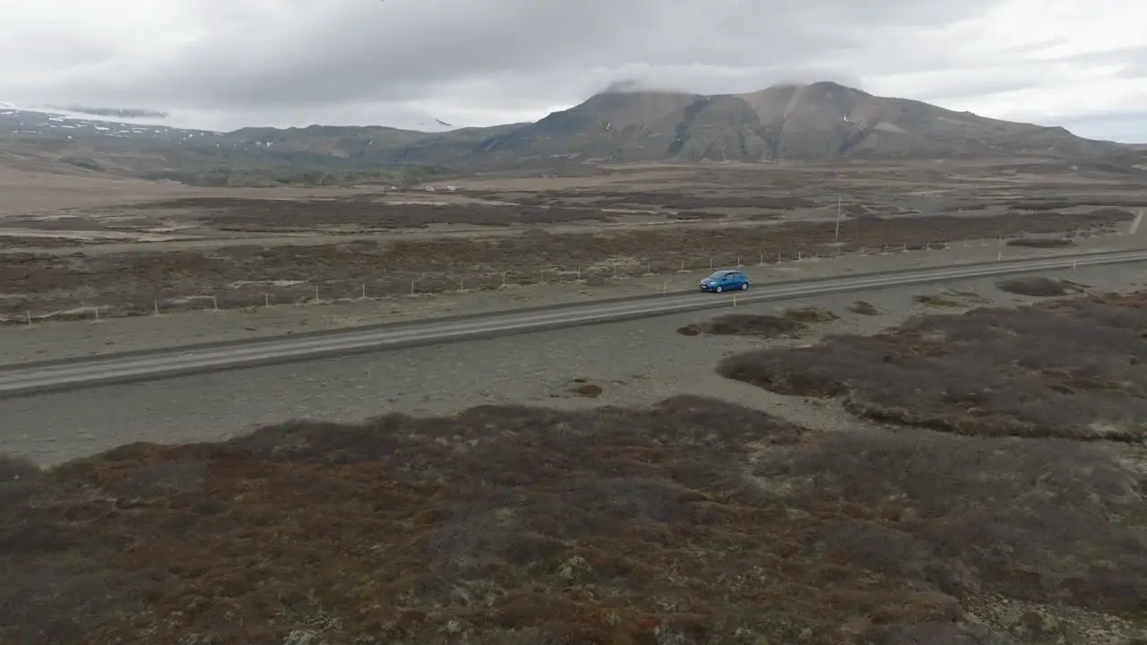 aerial view with tracking at medium distance to blue car and over the road leading to the icelandic rock formation of Hvitserkur on a dull day