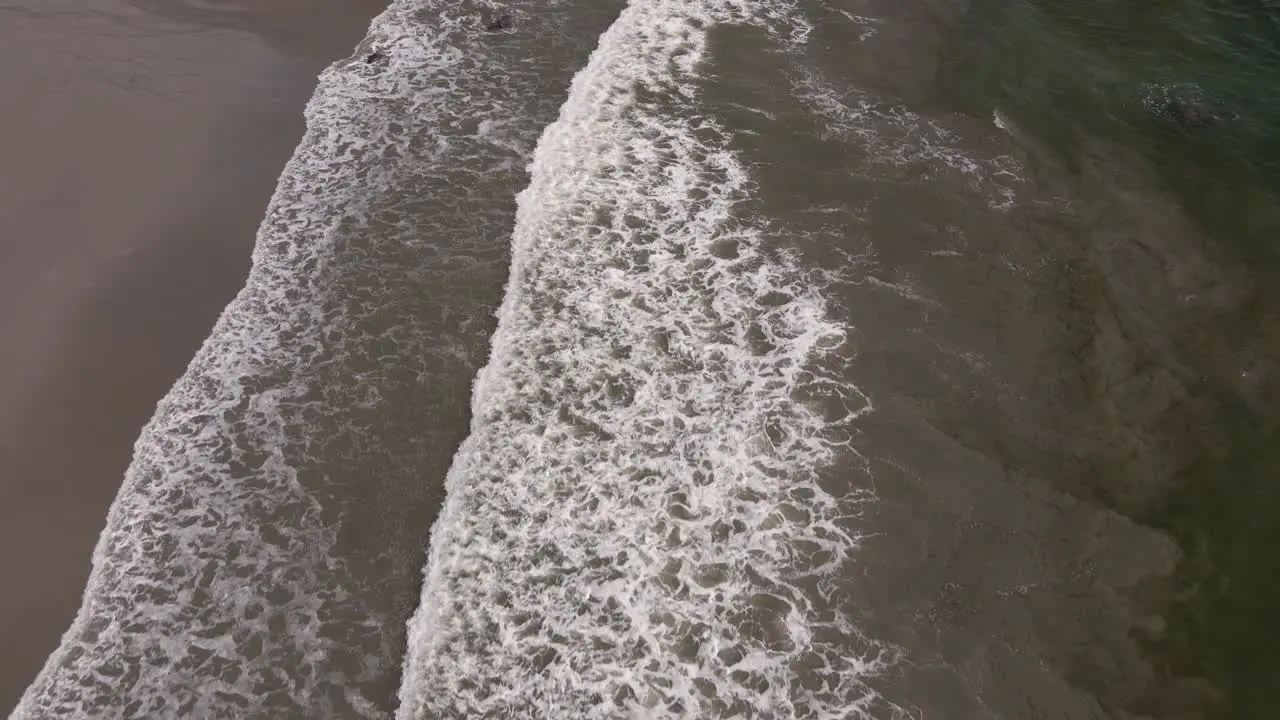 aerial view of foaming waves of the pacific ocean hitting the sandy beach