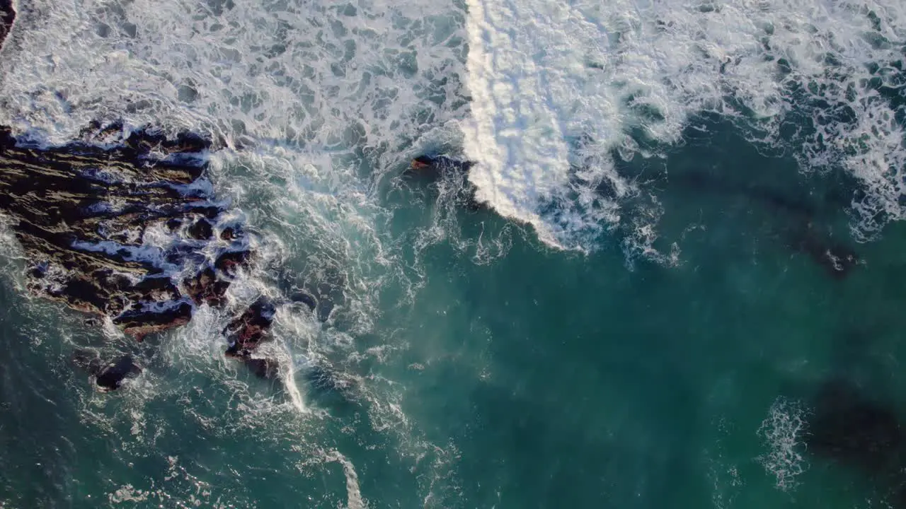 Waves break on rocky coastline top down aearial drone abstract view