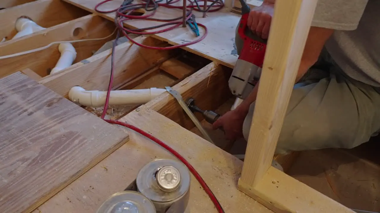 Plumber drilling through floor joists