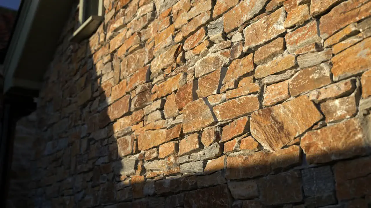 Parallax movement as sunset golden hour light hitting the side of a rustic stone walled building casting harsh shadows with luxury feel