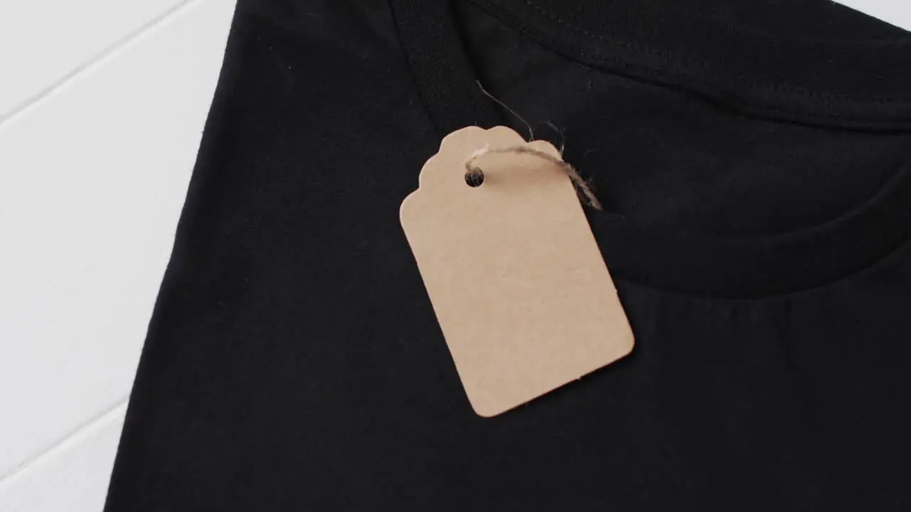 Video of flat lay of black t shirt with tag and copy space on white background