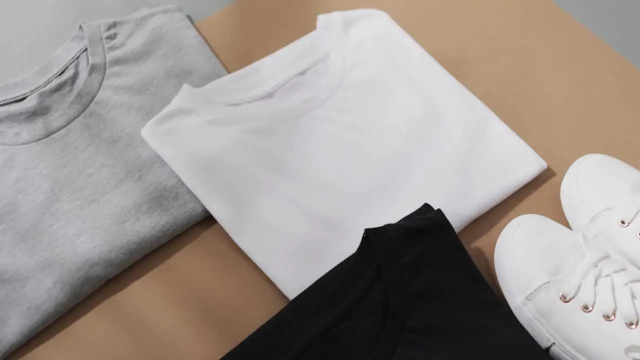 Video of flat lay of multi coloured t shirts and sneakers with copy space on brown background