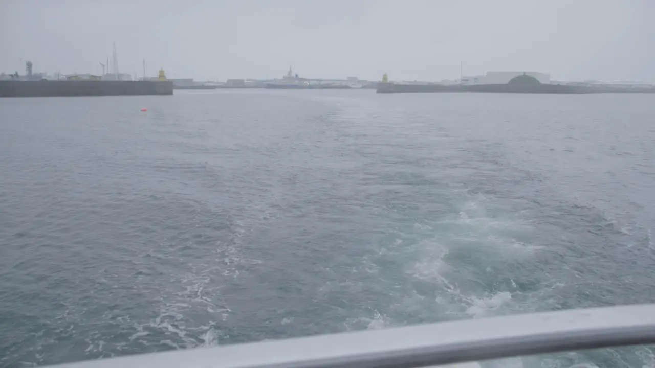 Floating away from Reykjavik harbor on cloudy day seen from stern of yacht