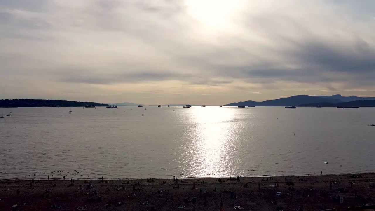 Summer sunset aerial fly over residential private beach at commercial industrial harbor with freightors barges cargo boats line up for iport export trade and recreational vessels parked 1-2