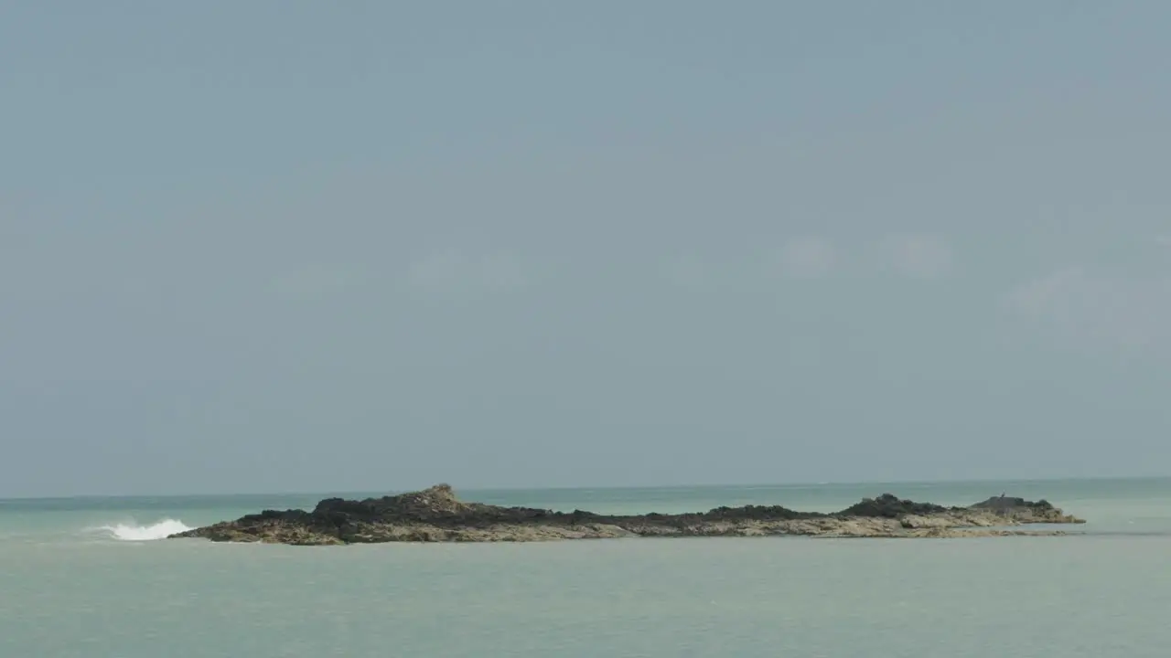 Wave crest carried by summer breeze and small rocky island on a sunny clear day