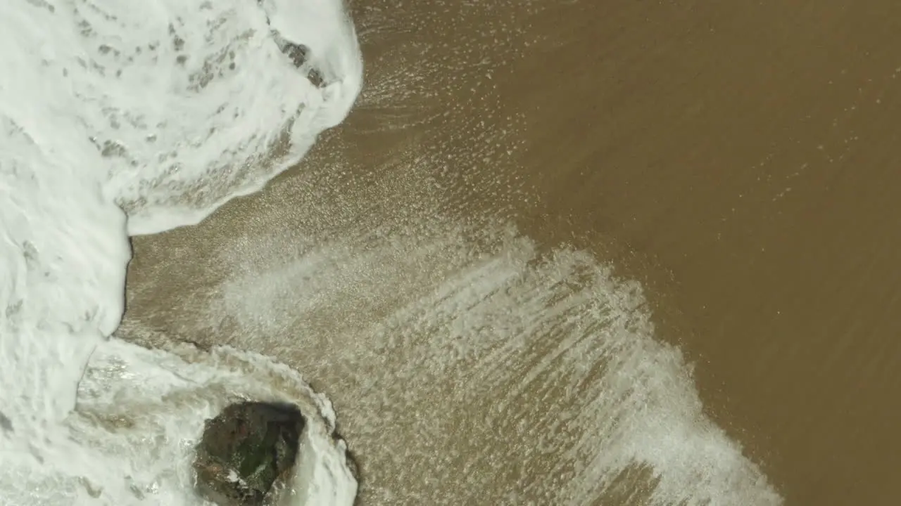 Rising aerial shot of foamy waves rushing over the sandy beach