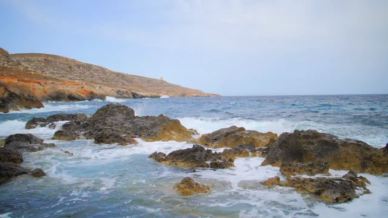 Massive waves and whitewash smashing into beach rocks and cliffs in slow motion alongside rocky coast of Ghar Lapsi Malta