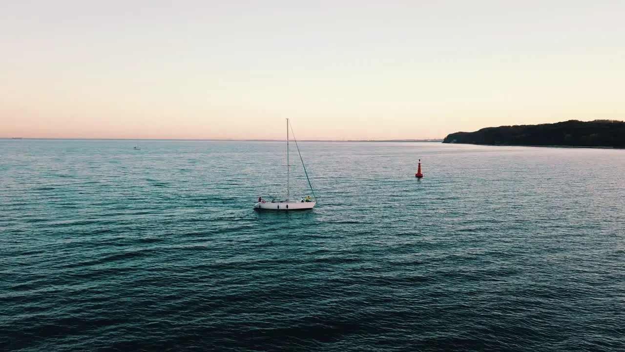 Drone flying above the yacht sailing into the bay at the sunset