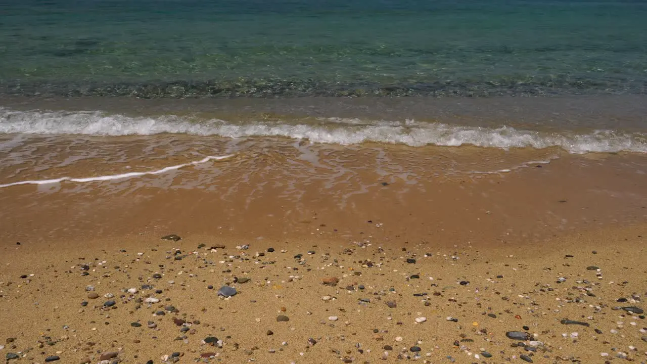 Gentle waves wash on a golden beach with small smooth scattered stones