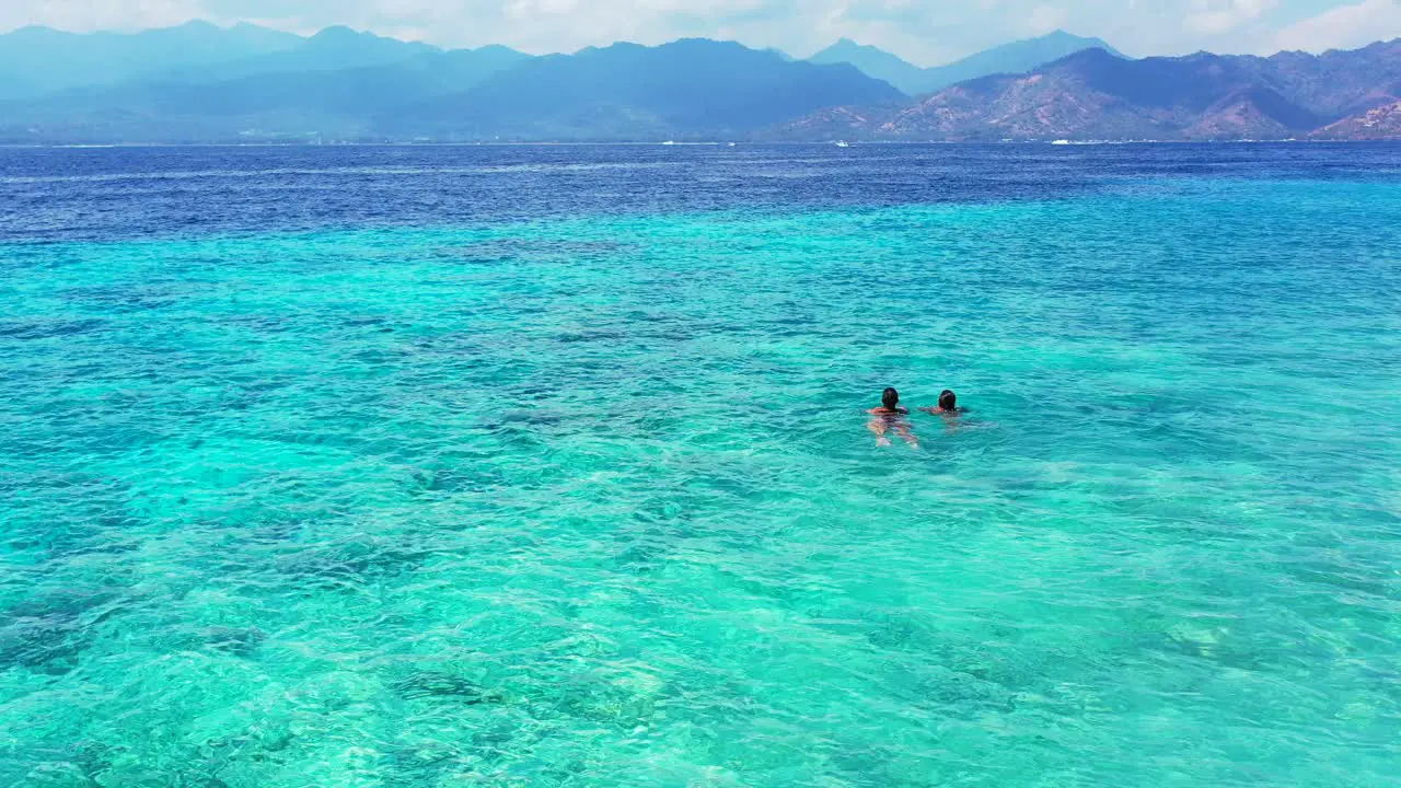 Two young female teenagers swimming in the crystal clear aqua water in perfect tourist holiday destination Indonesia