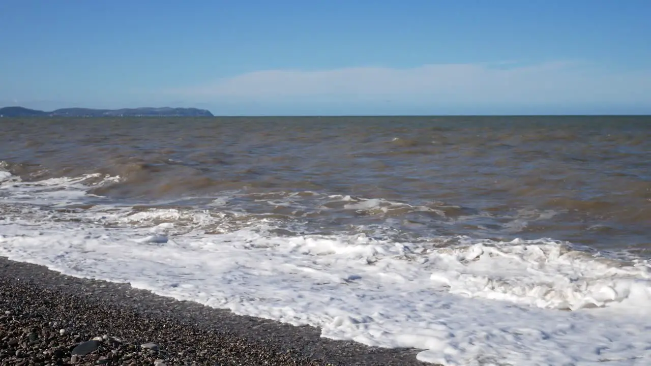 Stormy windy ocean waves barrel onto pebble beach Welsh coastline shore