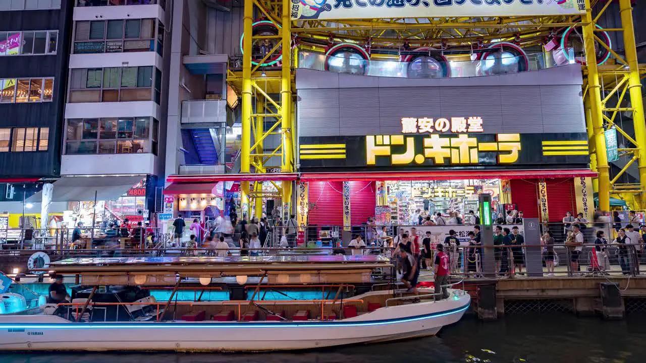 Night time lapse of people getting on tour boats outside the Ebisu Tower Ferris Wheel Don Quixote at the Dotonbori Canal Namba Osaka Japan