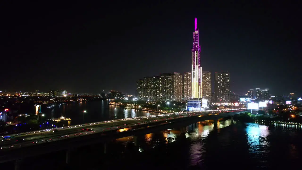 aerial dolly right with traffic speeding fast over the bridge and modern tall skyline in background at night in Ho Chi Minh City Vietnam