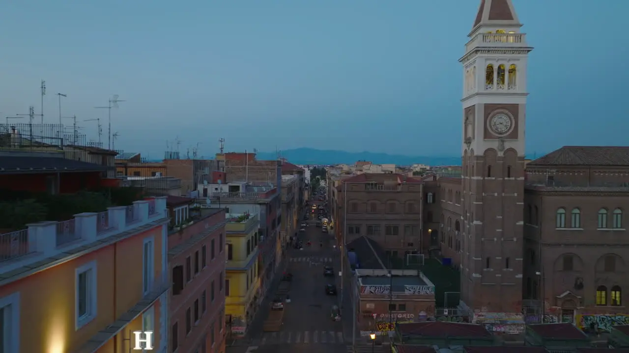 Fly around tower and surrounding historic buildings in city Forwards fly above street with parked cars after sunset Rome Italy