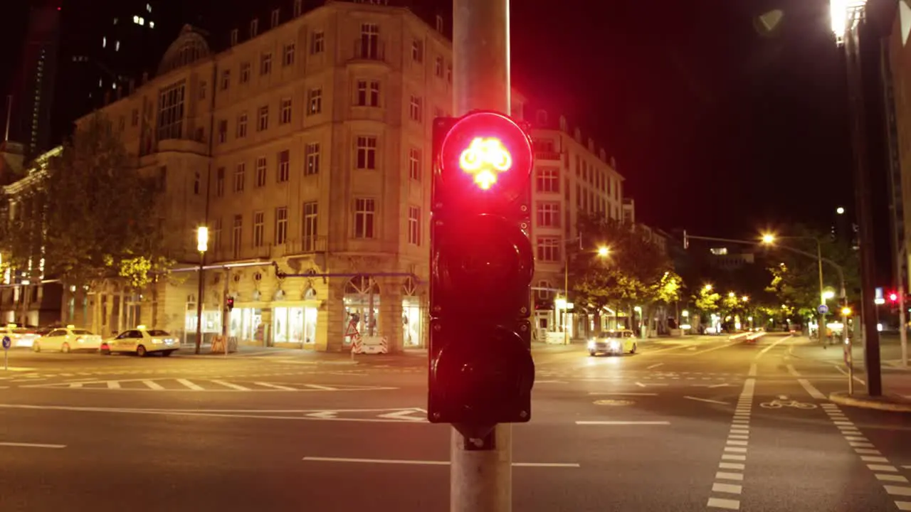 Through the pedestrian's perspective this timelapse captures a city street at night marked by colorful traffic light lined buildings trees streetlights and blurred vehicles due to long exposure