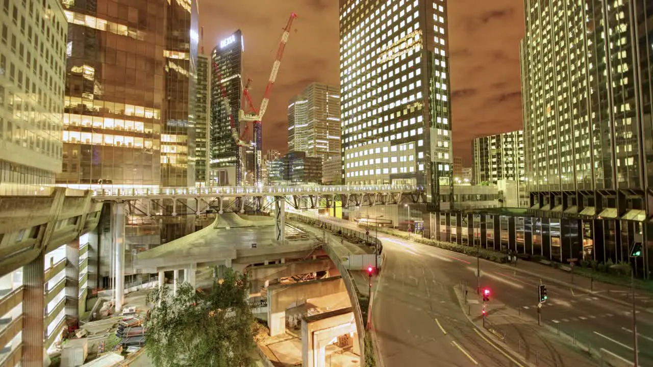 A captivating timelapse unveils an intricate cityscape at night teeming with tall buildings of assorted designs alongside a bustling highway arched over an active construction site