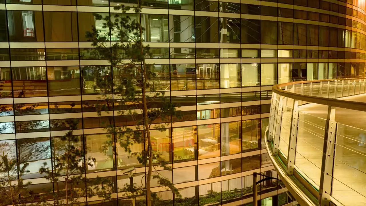 Timelapse reveals a modern building at night with a curved glass facade reflecting the orange glow from the street lights and a balcony with glass railing