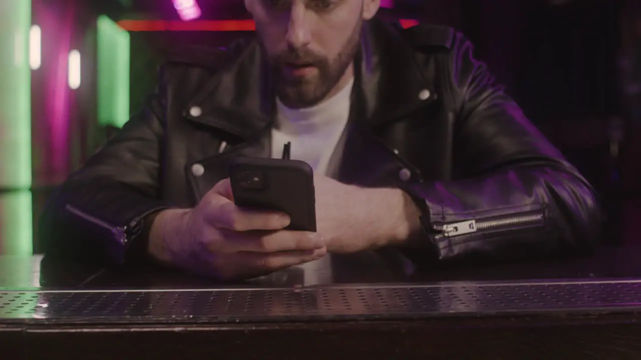 Close Up Of A Bearded Man Using Mobile Phone And Drinking While Sitting At Bar Counter