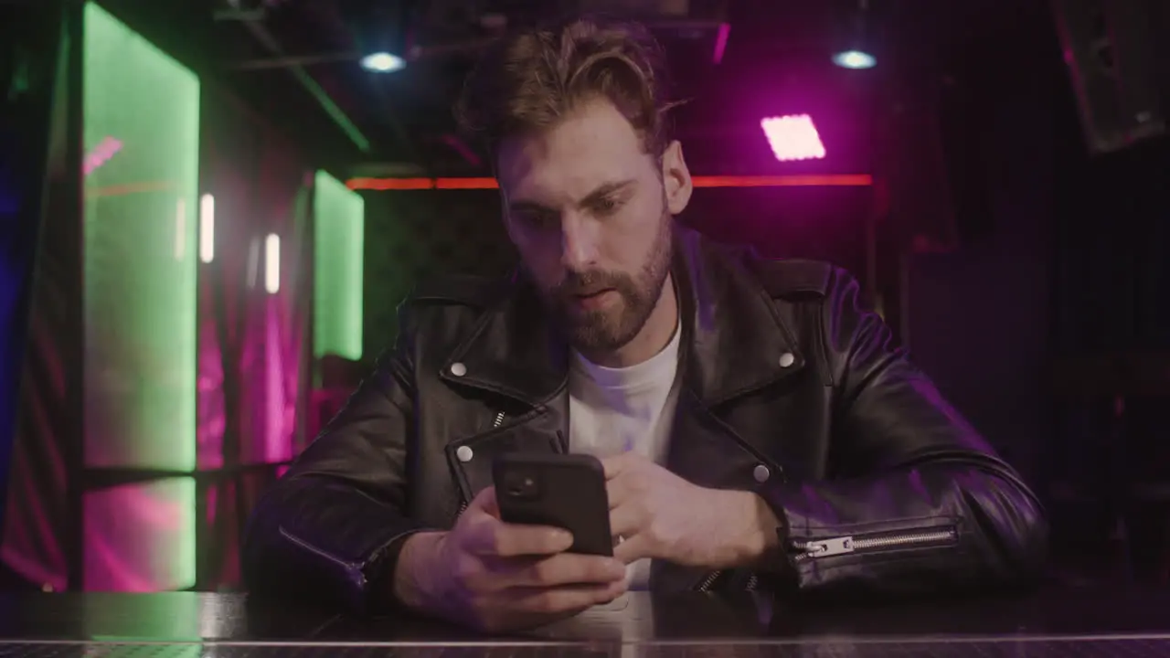 Serious Bearded Man Drinking And Using Mobile Phone While Sitting At Bar Counter