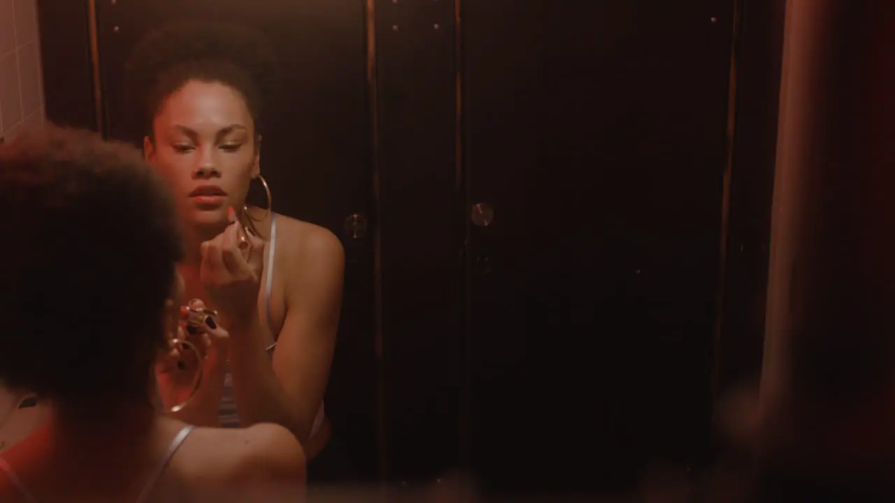 Beautiful Girl Looking At Mirror And Putting Lipstick On While Her Friend Washing Hands After Using The Bar Toilet