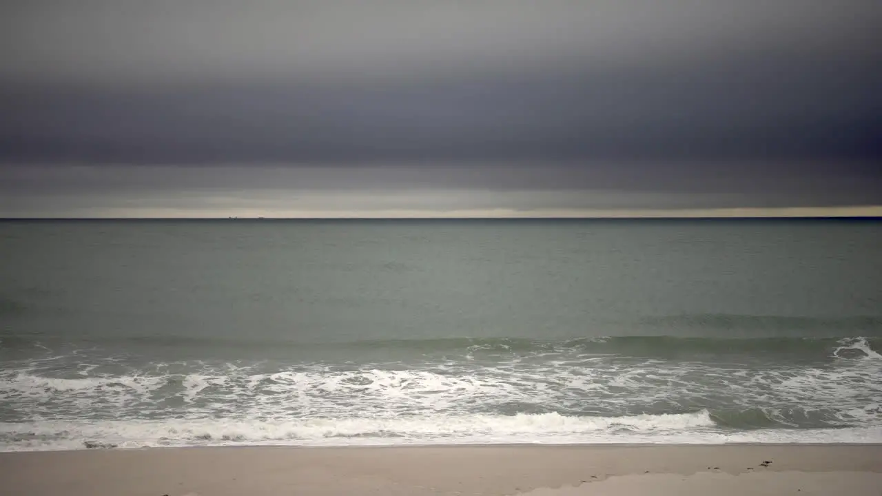 Waves crash onto a shoreline while moody clouds pass over