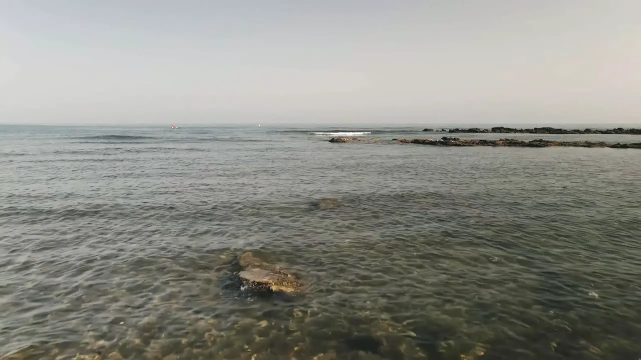 Forward dolly shot from a rocky beach into the clear water