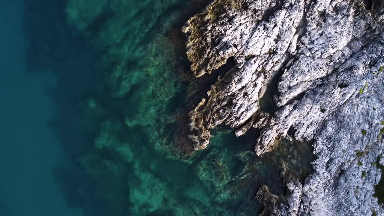 Rocky shore with calm crystal clear blue water top down