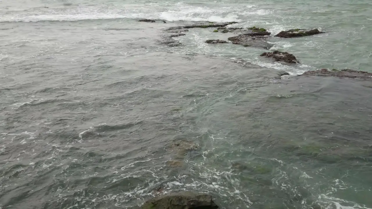 Ocean waves roll onto shallow rocky shore on coast static shot