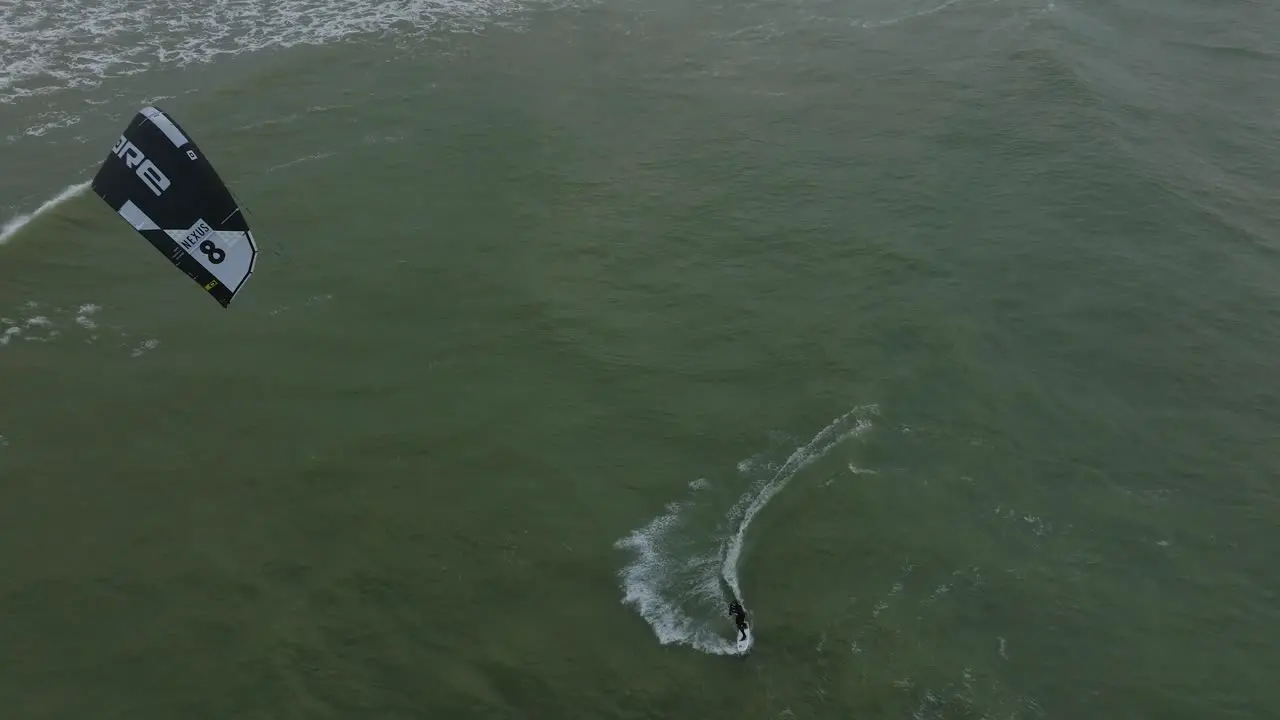 Establishing aerial view of a man engaged in kitesurfing overcast winter day high waves extreme sport Baltic Sea Karosta beach  drone birdseye shot moving forward