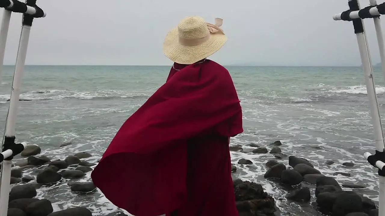 Islamic woman wearing burqa during holiday at rocky beach puts on straw hat