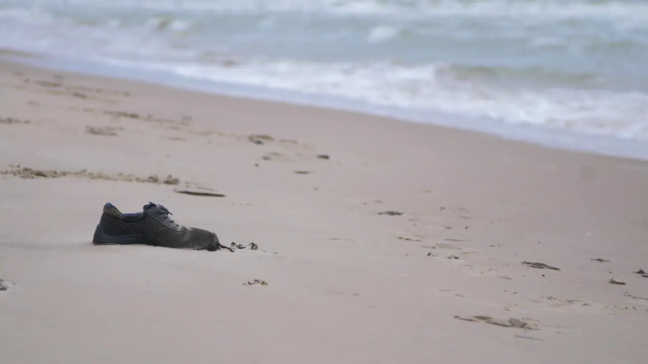 Black shoe on the beach trash and waste litter on an empty Baltic sea white sand beach environmental pollution problem overcast day medium shot