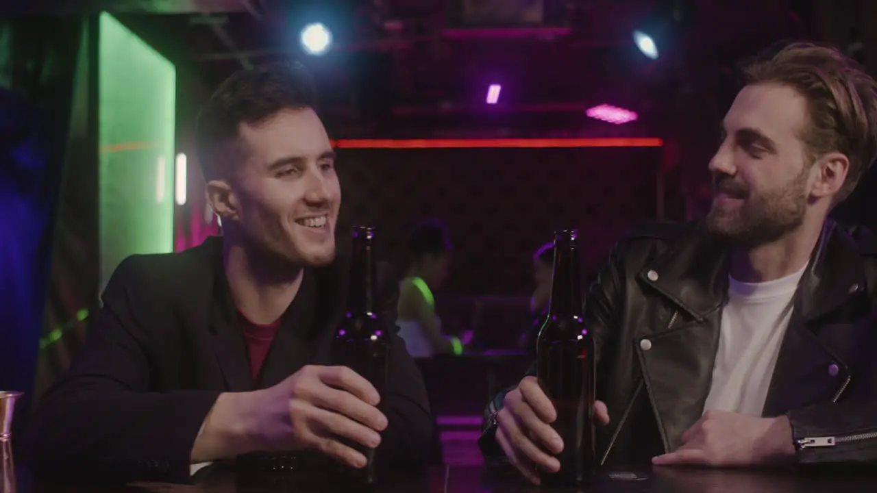 Two Male Friends Toasting And Drinking Beer While Sitting At Bar Counter