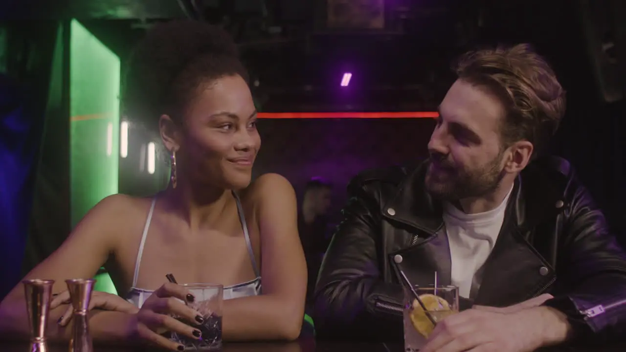 Multiethnic Couple Holding Drinks And Smiling At Camera While Sitting At Bar Counter