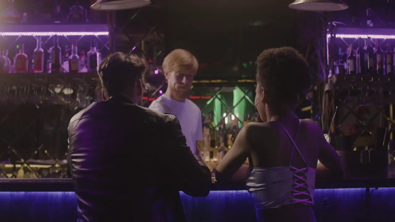 Waiter Serving Drinks To Multiethnic Couple Sitting At Bar Counter