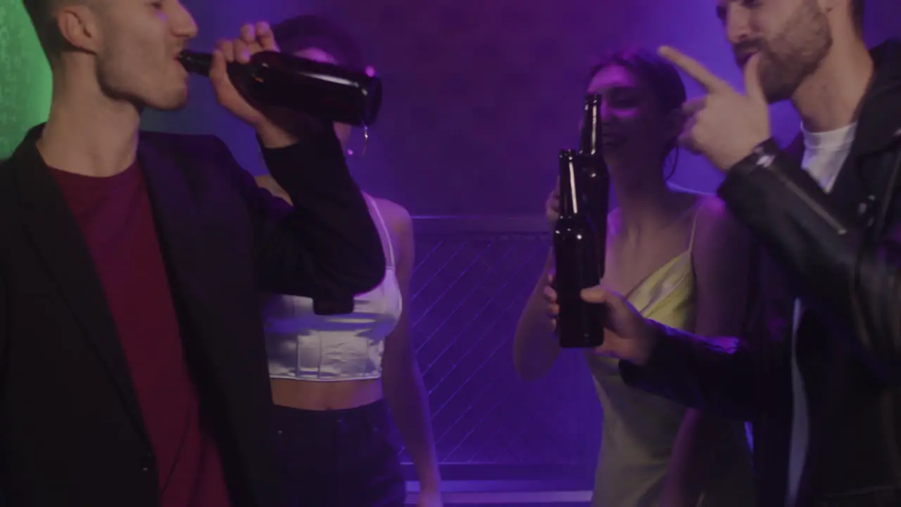 Group Of Four Young Friends Toasting With Beer Bottle While Dancing At Disco