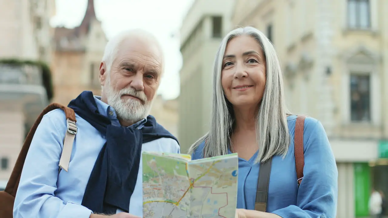 Portrait Of A Senior Couple Of Tourists Standing In The City And Looking At A Map Then Smiling To The Camera