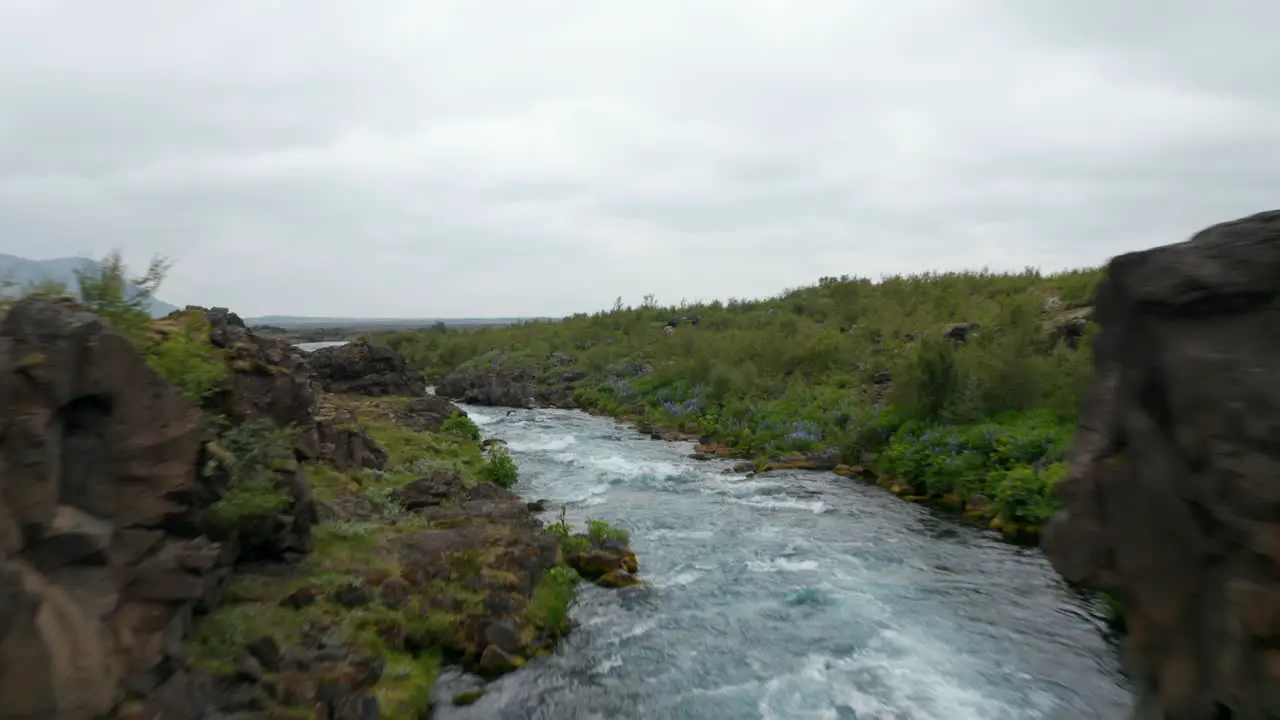 Aerial view drone flying under bridge over flowing river in rocky countryside in Iceland Birds eye spectacular icelandic highlands with river powerfully flowing