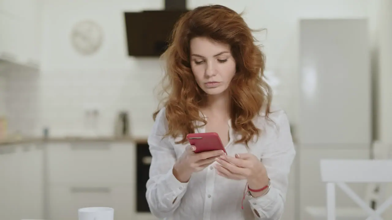 Serious woman taking phone at open kitchen Young lady closing laptop at home