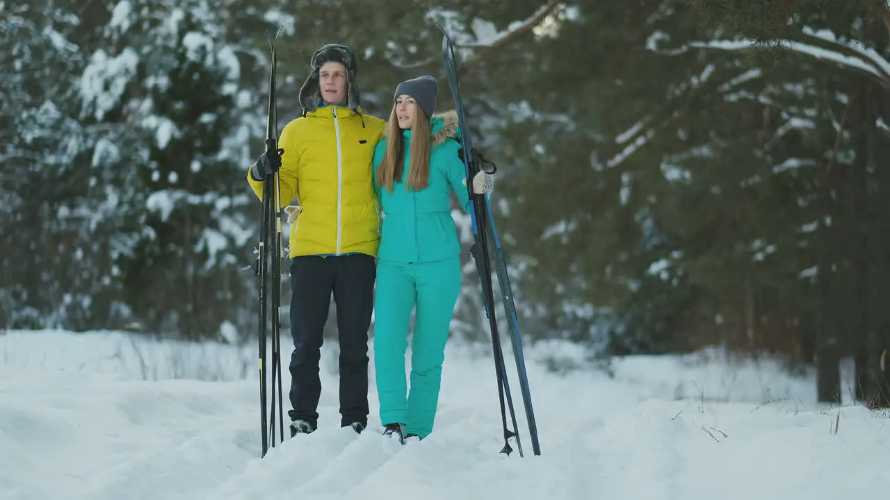 Side view portrait of active young couple carrying skis chatting on the way back in beautiful winter forest copy space