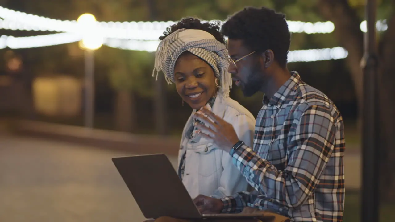 Black Man and Woman Using Laptop and Chatting in Park in Evening