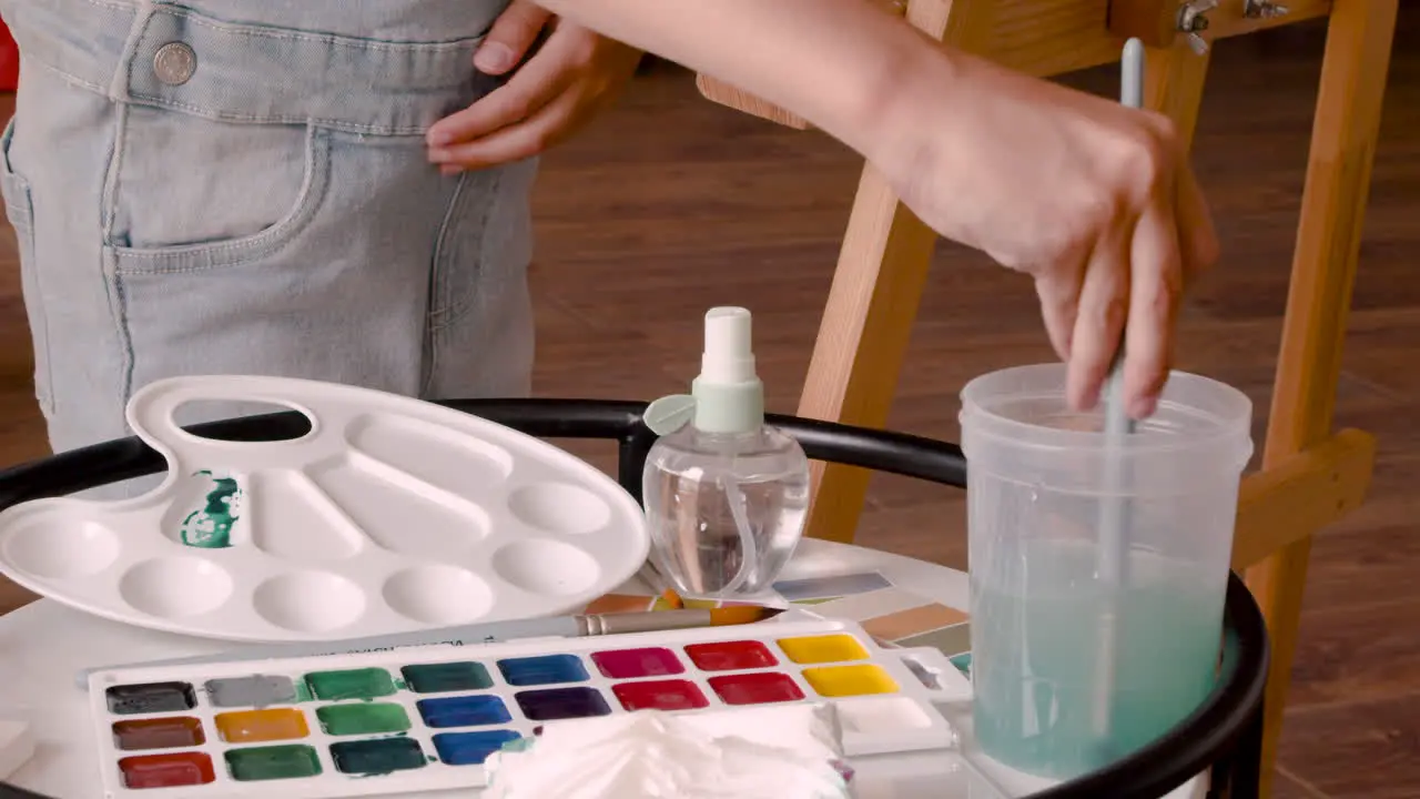 Close Up View Of A Girl's Hands Wetting The Brush With Water And Mixing It With Green Paint