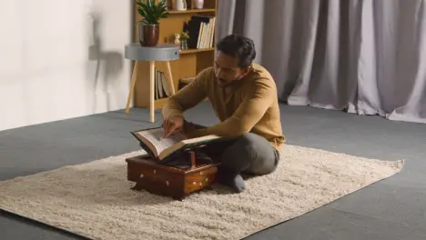 Muslim Man At Home Sitting On Floor And Reciting From The Quran 2