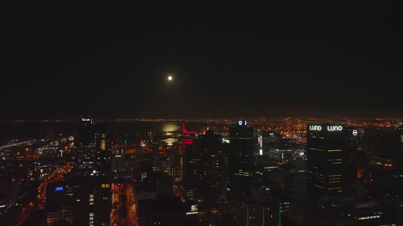 Aerial descending footage of night in central part of city Tall business buildings and water surface in sea bay reflecting moonlight Cape Town South Africa