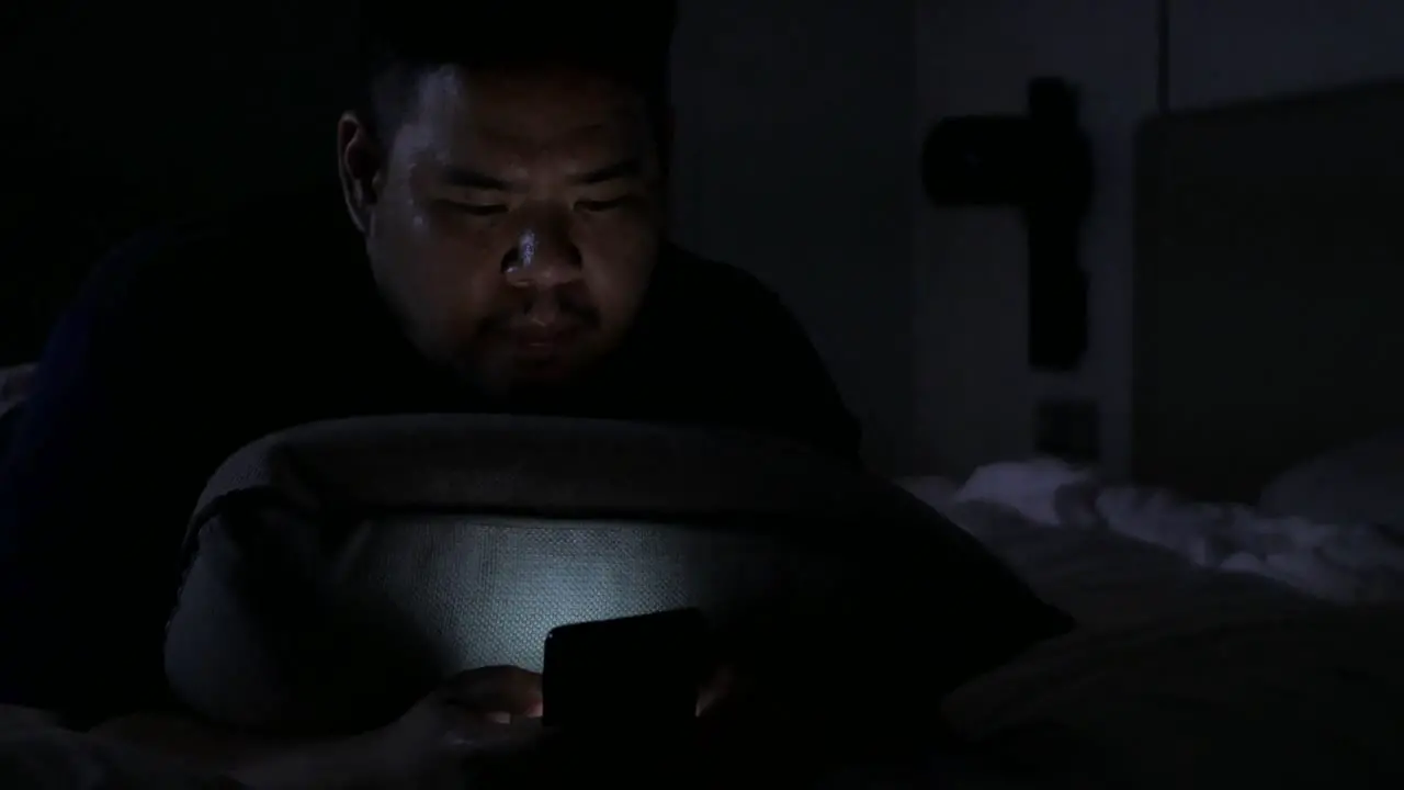 asian man while chatting on mobile phone and lay on the bed in bed room in night time