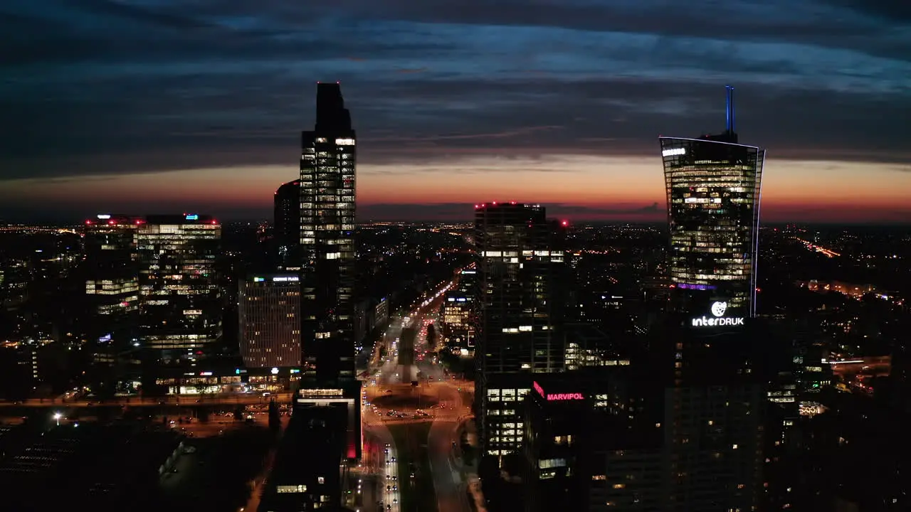 Aerial panoramic descending footage of modern skyscrapers against colourful sunset sky Silhouette of high rise buildings with lighted windows Warsaw Poland