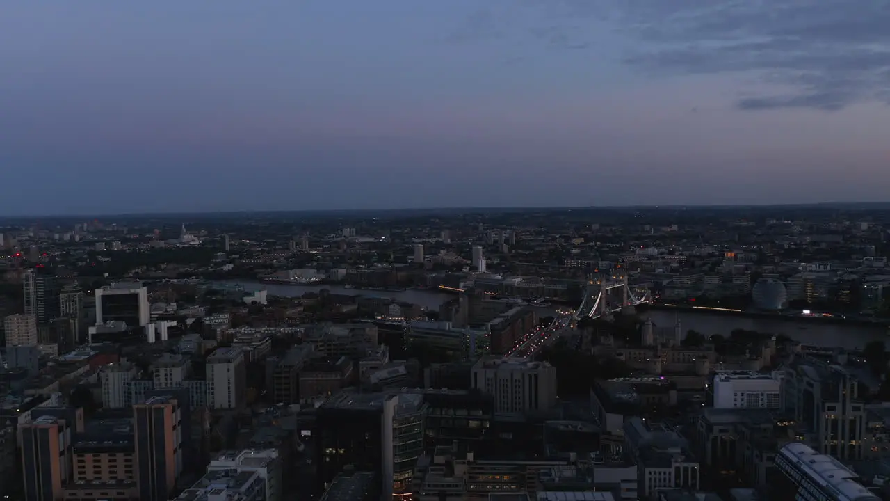 Forwards fly above urban borough after sunset Heading towards illuminated Tower Bridge over River Thames London UK