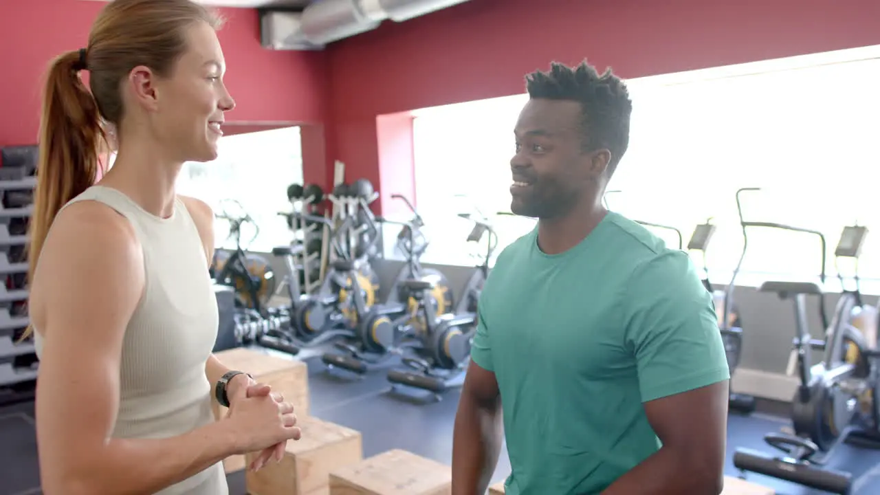 Fit young Caucasian woman and African American man pose in a gym