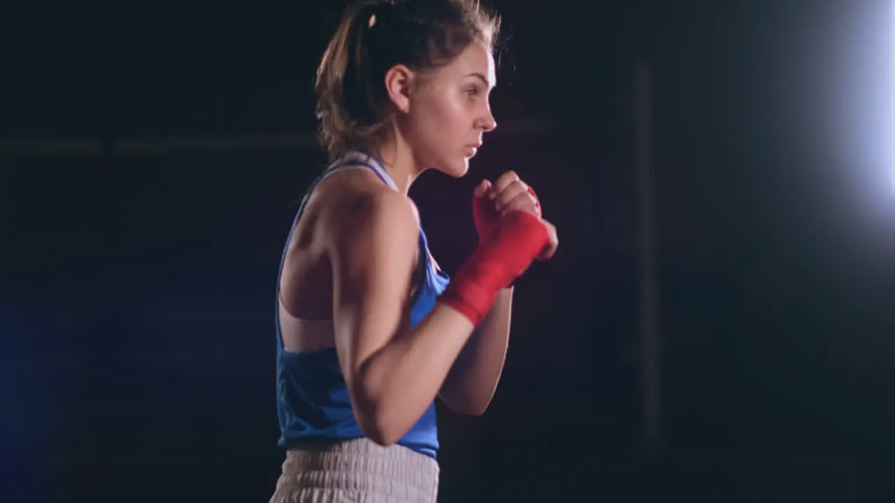 Female boxer training in dark room with backlight in slow motion side view steadicam shot