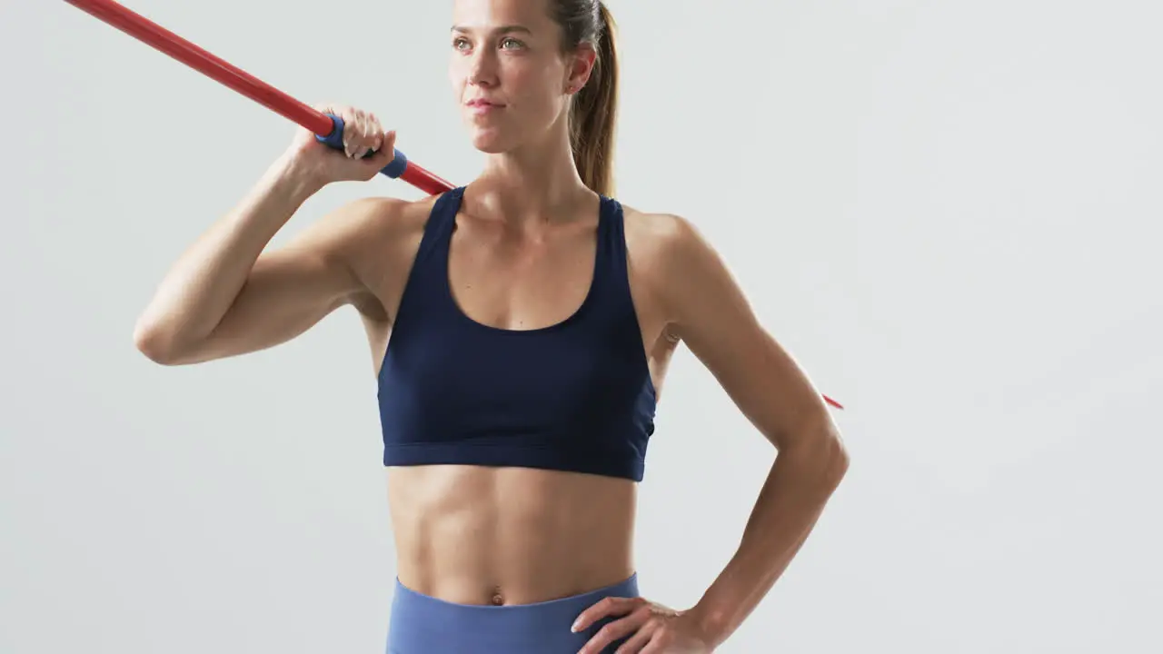 Young Caucasian woman athlete holds a javelin at the gym on a white background